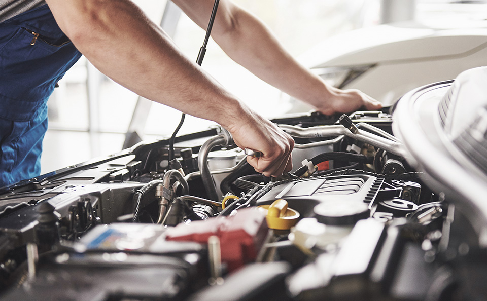 Close-up of a certified GMC Service Center mechanic's body and arms and hands as he inspects an engine.